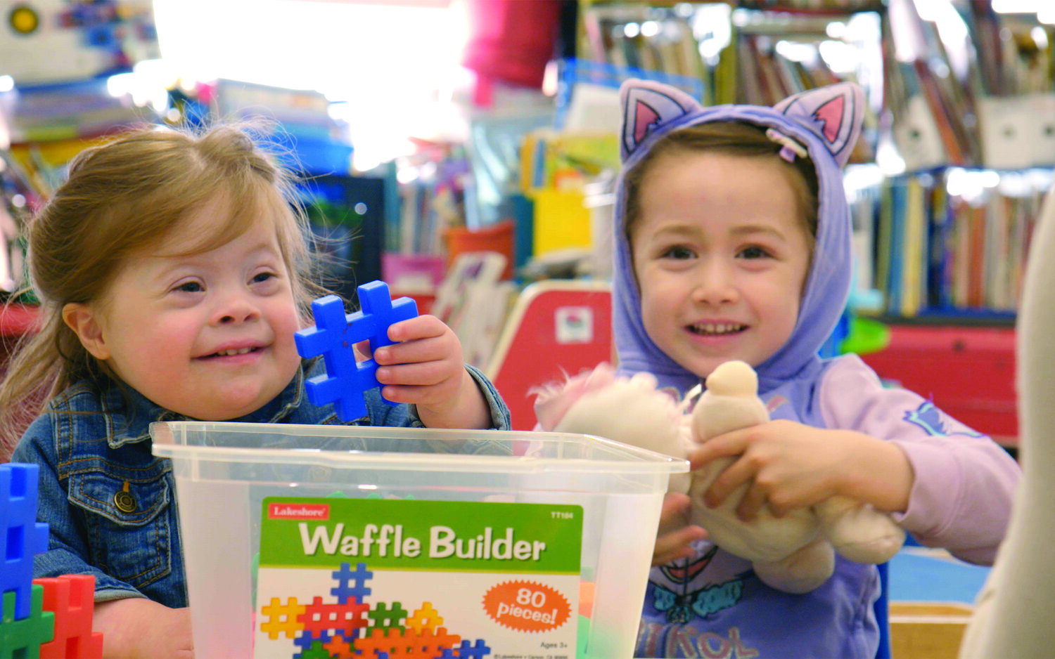 Two young students, one with down syndrome, sit at a desk playing